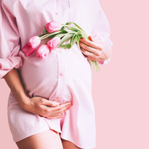 Pregnancy, Motherhood, Mother's Day Holiday concept. Young woman in maternity shirt dress with tulips flowers holds hands on belly. Beautiful pregnant woman waiting for baby birth. Pregnancy, Motherhood, Mother's Day Holiday concept. Young woman in maternity shirt dress with tulips flowers holds hands on belly. Beautiful pregnant woman waiting for baby birth.