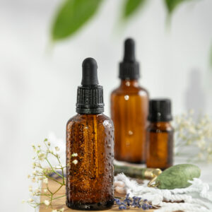 Bottles of dark amber glass with essential oil, massage jade roller and tropical leaves Bottles of dark amber glass with essential oil, massage jade roller and tropical leaves on wooden bench. Natural organic cosmetic, aromatherapy, message oil.